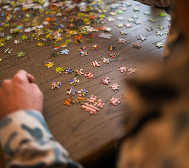 Puzzle pieces spread across a table as people work on a jigsaw puzzle.
