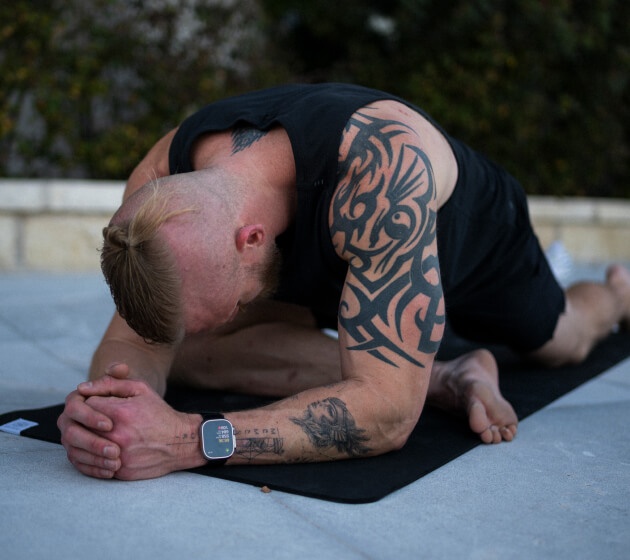 A man stretches on a yoga mat outdoors, resting on his forearms.