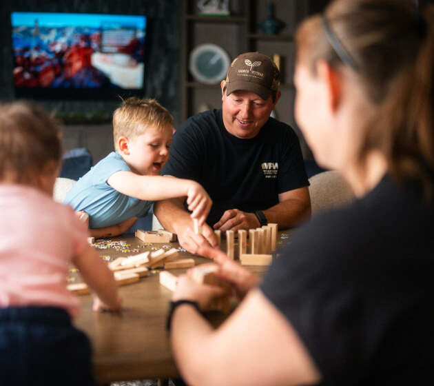 An adult and children sit at a table building with wooden blocks.