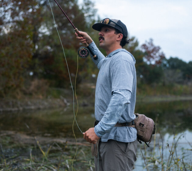 A person fishes along the edge of a river outdoors.