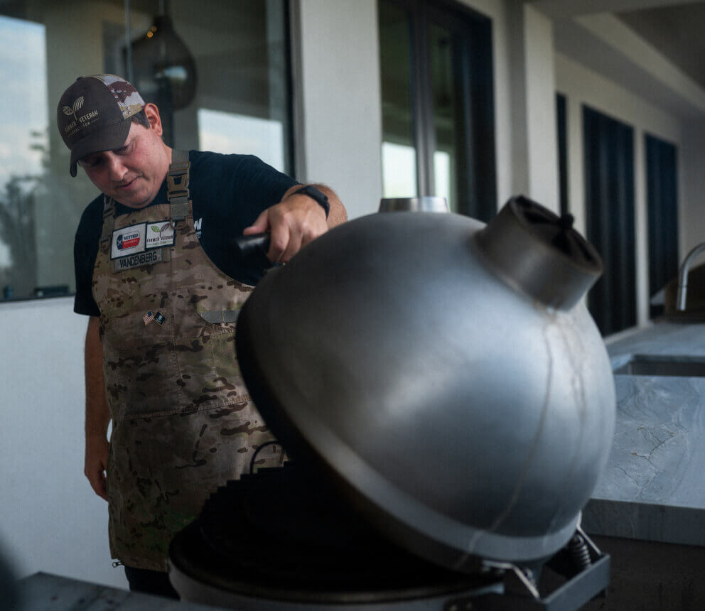 A person opens the lid of an outdoor grill while cooking.