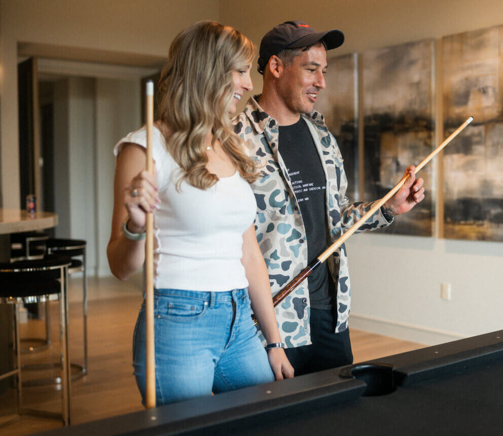 Two people stand indoors holding pool cues at a billiards table.