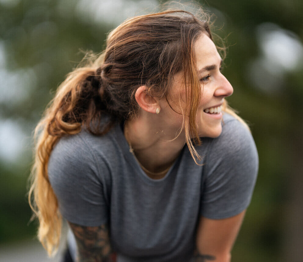 A woman outdoors smiles while leaning forward.