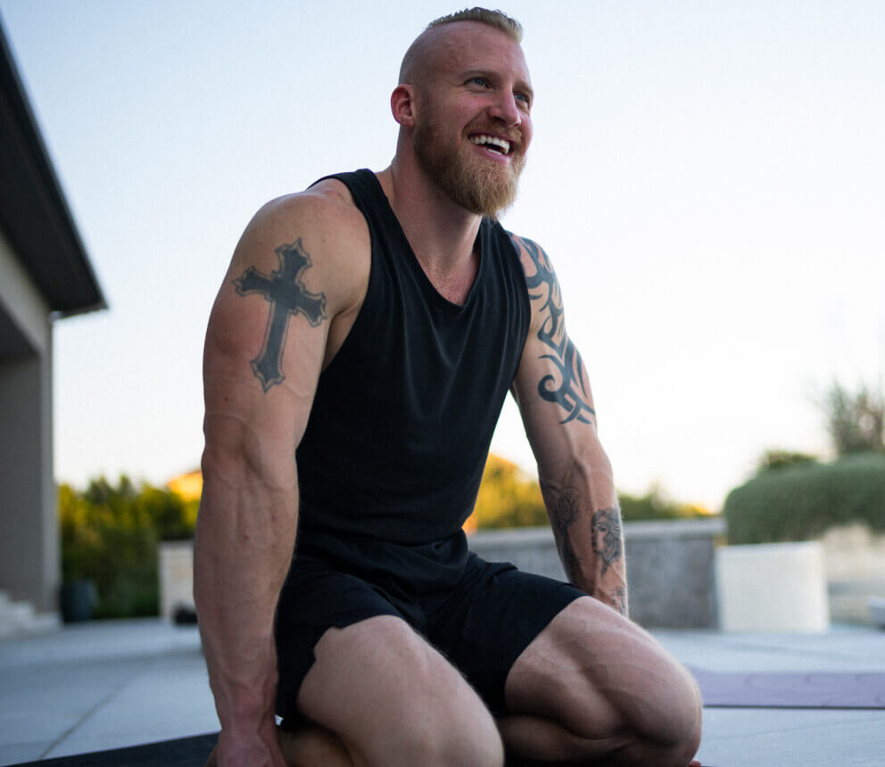 A man kneels outdoors on a mat, smiling after a workout.