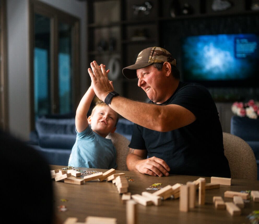 An adult and a young child high-five while sitting at a table with wooden blocks.
