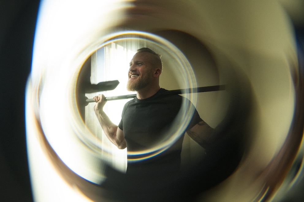 A man stands, smiling, holding a squat bar on his shoulders.