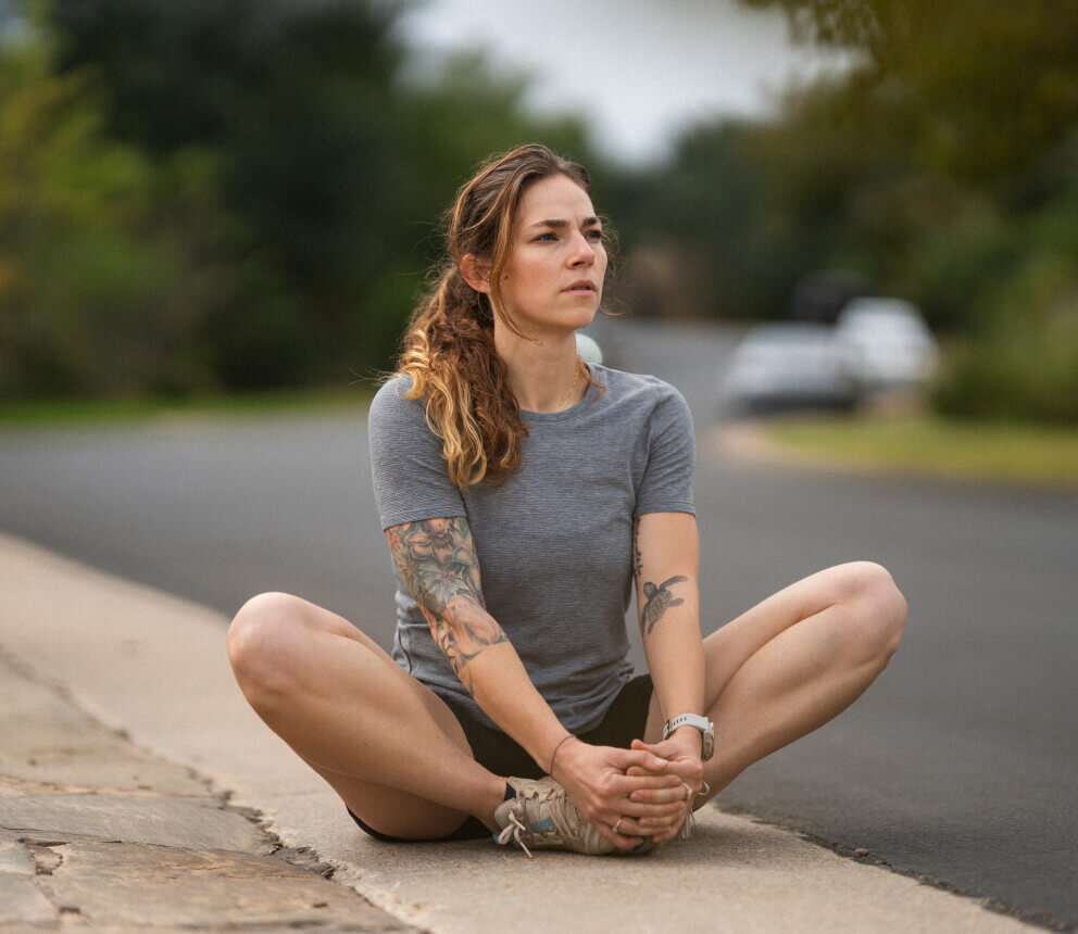 A woman sits on the curb stretching her legs on a quiet street.